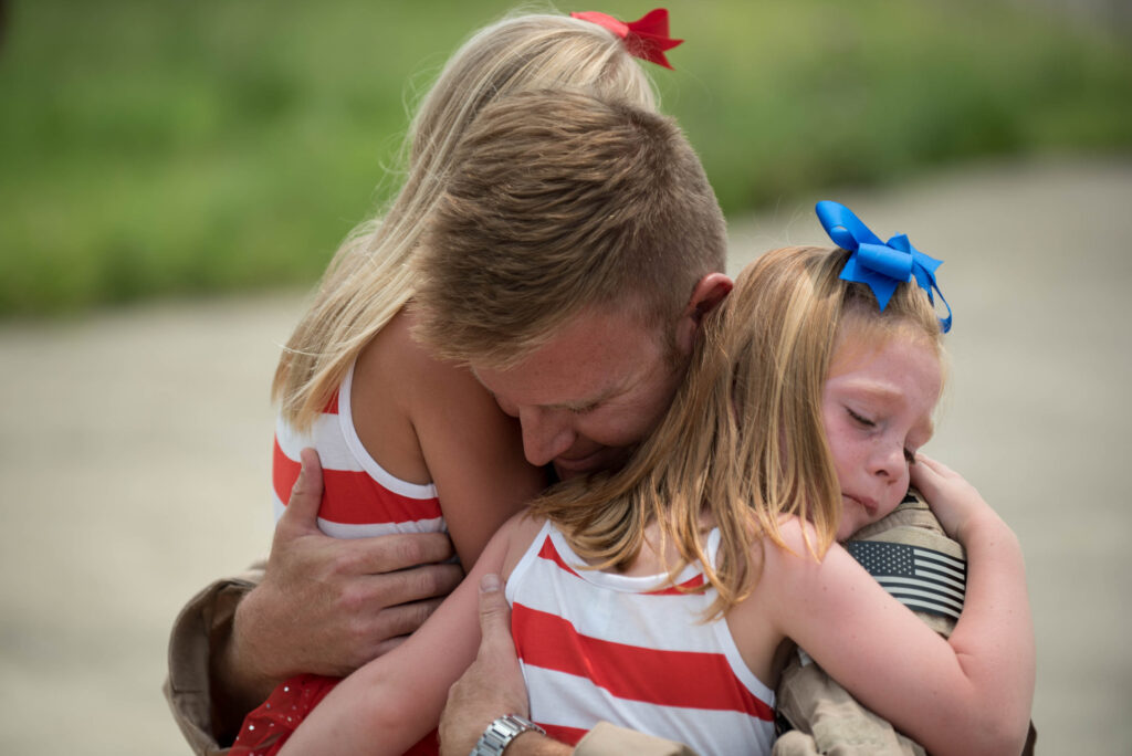 Military service member in uniform hugging his two daughters outdoors during a homecoming, representing military and veteran families welcome at Starlight Horizon