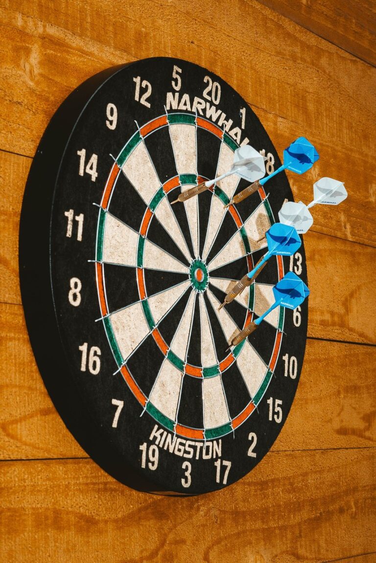 Dartboard mounted on a wood-paneled wall with several blue and white flighted darts clustered near the bullseye
