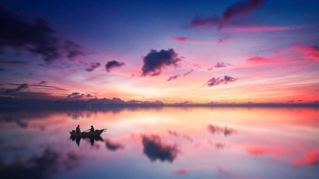 Two anglers fishing from a small boat on calm water at sunset