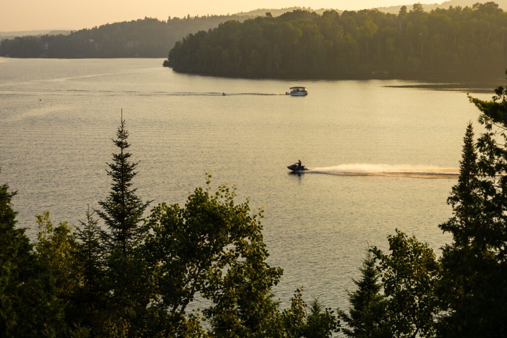 Jet ski crossing a calm lake at golden hour with wooded shoreline