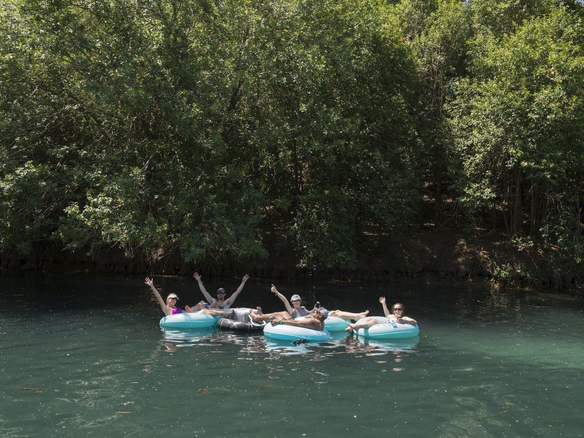Group of friends raising their arms while tubing the Comal River in New Braunfels Texas
